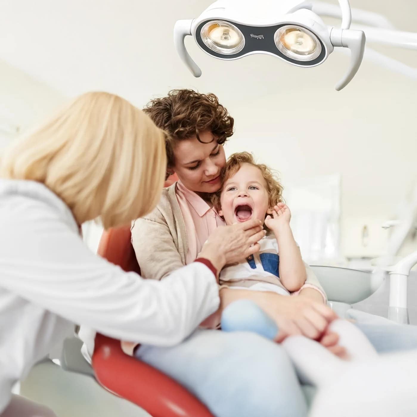 Friendly dentist examining a young patient while her mother comforts her